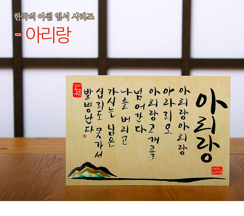 [텍스트: 한국의 아침 엽서 시리즈 - 아리랑 / 한국의 선물 아침 / 아리랑 아리랑 아라리요 아리랑 고개를 넘어간다 나를 버리고 가시는 님은 십리도 못가서 발병난다 / made in Korea] 한지 질감 베이지 바탕에 흑색 붓글씨 아리랑 가사와 좌하단 산수 수묵채색 산악 문양 구성 엽서형 디자인