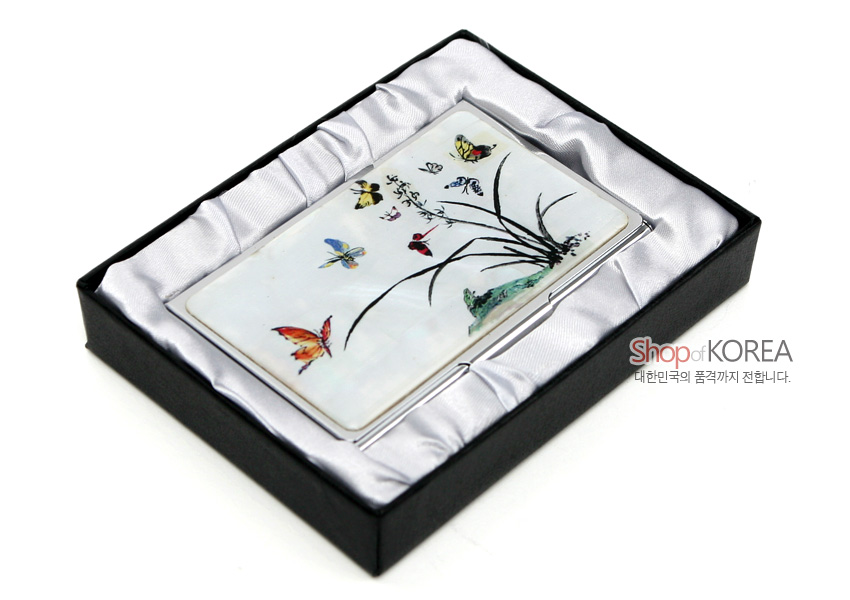 [텍스트: Shop of KOREA 대한민국의 품격까지 전합니다.] 자개 바탕 위에 옻칠 기법으로 그린 난초와 다채로운 나비 문양, 은색 금속 테두리의 직사각 명함케이스가 실크 패브릭 내장 박스에 놓인 모습
