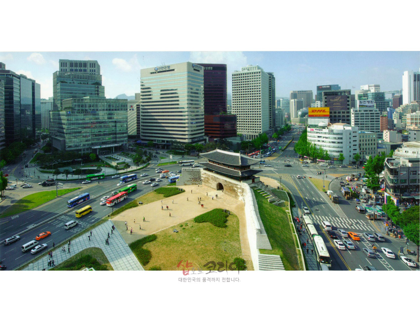 [텍스트: 대한민국의 품격까지 전합니다.] 푸른 하늘 아래 석조 성곽과 기와지붕 남대문, 회색·유리 외벽 고층빌딩과 도로가 대조되는 서울 도심 전경 엽서 이미지