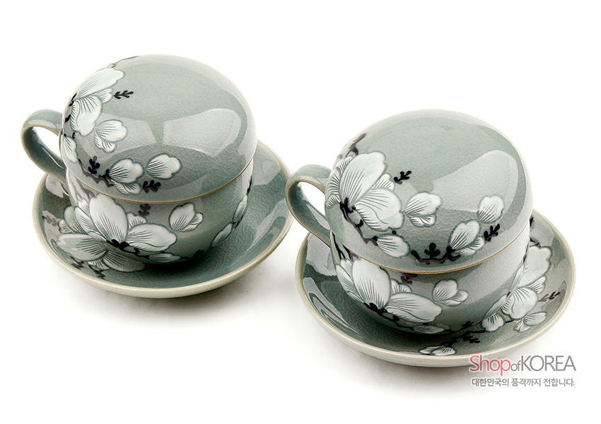 [텍스트: Shop of KOREA / 대한민국의 품격까지 전합니다.] 옅은 비취색 청자 유약 위에 상감기법으로 표현된 백색 목련 화조문이 둘러진 뚜껑잔과 받침으로 구성된 2인용 도자기 다기세트 이미지 설명