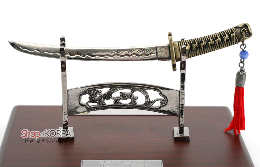 [텍스트: Shop of KOREA / 대한민국의 품격까지 전합니다 / MADE IN KOREA] 금속 재질 칼날과 손잡이, 파도형 음각 문양, 청색 구슬과 붉은 술 매듭 장식, 목재 받침대와 전통 문양 스탠드 조화 장식품