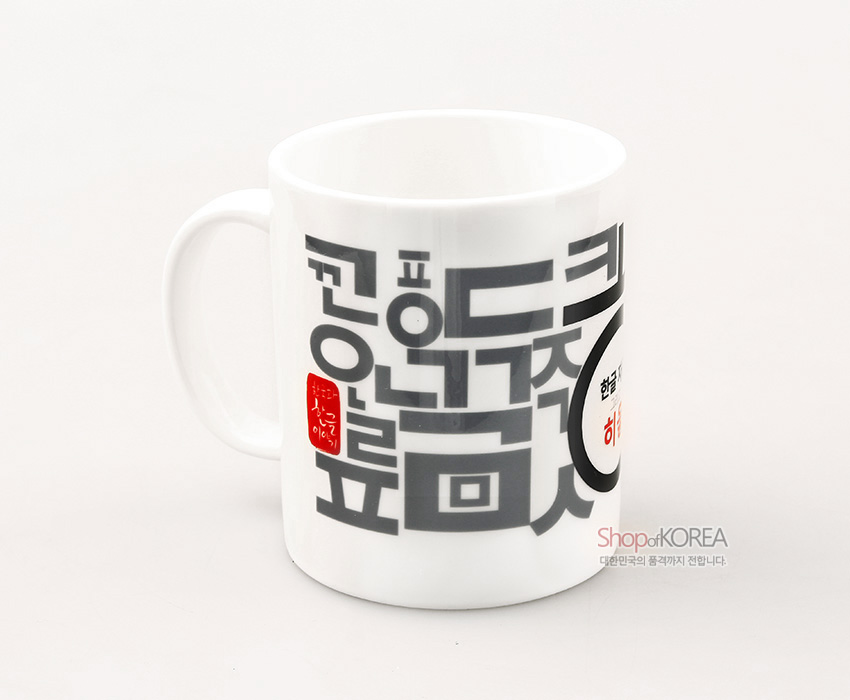 [텍스트: 한글 하늘에서 이룬 큰 뜻 Shop of KOREA 대한민국의 품격까지 전합니다] 백색 도자 머그컵에 짙은 회색 한글 자모를 기하학적으로 배열하고 붉은 인장과 포인트 글자를 더한 현대적 그래픽 디자인