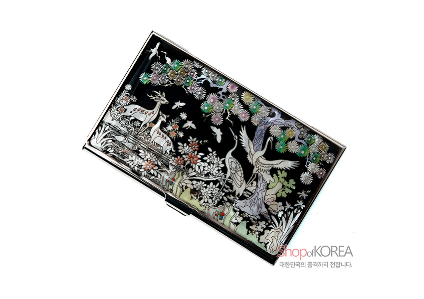 [텍스트: Shop of KOREA / 대한민국의 품격까지 전합니다.] 흑색 배경 금속 명함집 위 자개 상감 기법으로 장생도 학과 사슴, 소나무와 국화 문양을 섬세하게 표현한 디자인