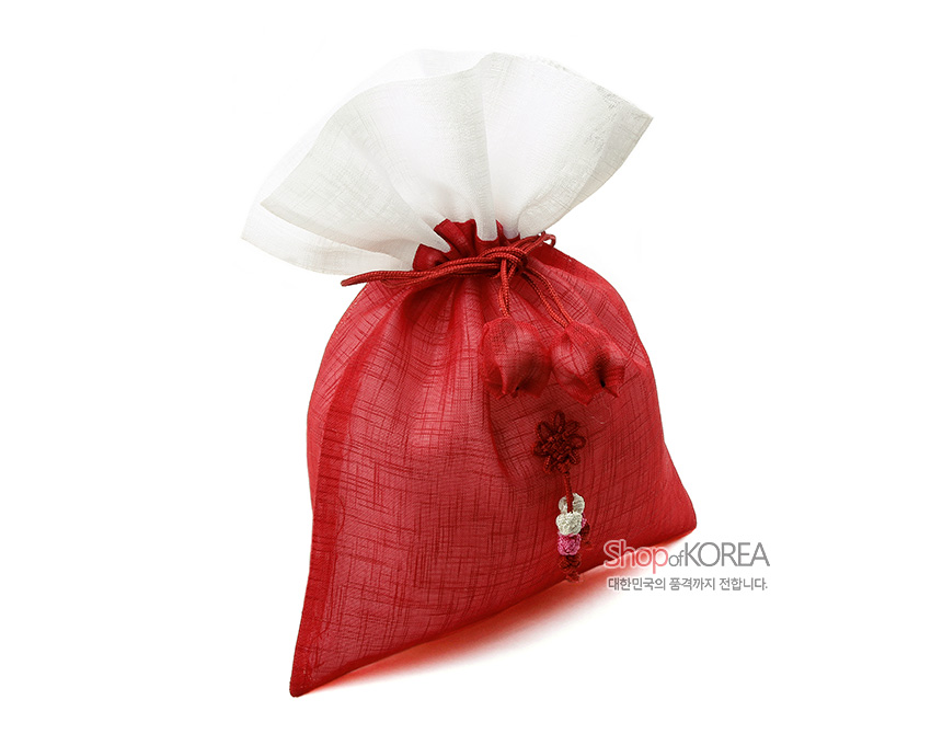 [텍스트: Shop of KOREA 대한민국의 품격까지 전합니다.] 붉은 모시와 상단 백색 모시 배색의 복주머니, 붉은 매듭 끈과 매달린 매듭 장식이 돋보이는 전통 공예품 형상