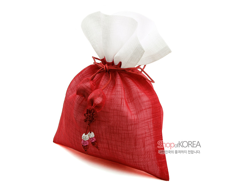 [텍스트: Shop of KOREA 대한민국의 품격까지 전합니다.] 붉은 모시 천과 백색 모시 상단 배색, 전통 매듭 기법으로 묶은 끈과 복숭아 모양 매듭장식이 어우러진 복주머니 형태 공예품 표현