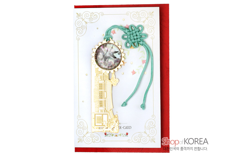[텍스트: Shop of KOREA] 금장 금속 소재에 기와집 형상과 자개 상감 쌍학 원형 장식, 청록색 전통 매듭 끈이 어우러진 책갈피 이미지
