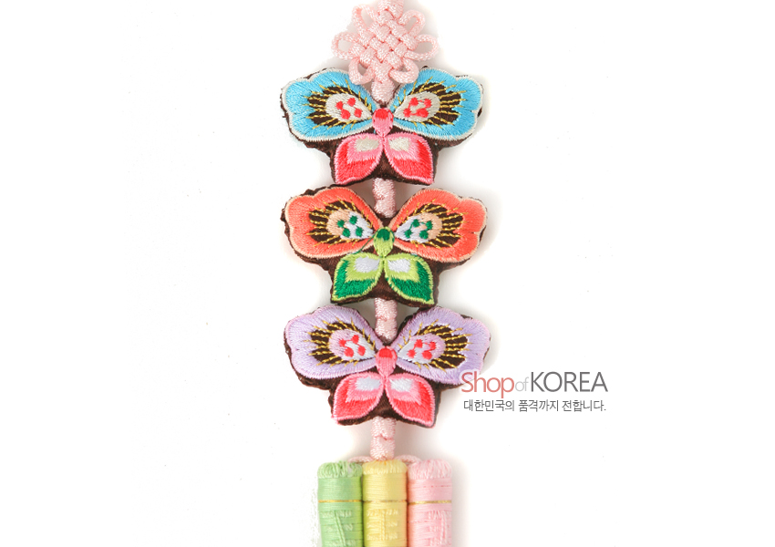 [텍스트: Shop of KOREA 대한민국의 품격까지 전합니다.] 분홍 매듭 위에 청록·분홍·보라 색실로 수놓은 나비 문양 3단 배열, 아래로 연두·노랑·분홍 비단 그라데이션 술 장식 노리개 이미지