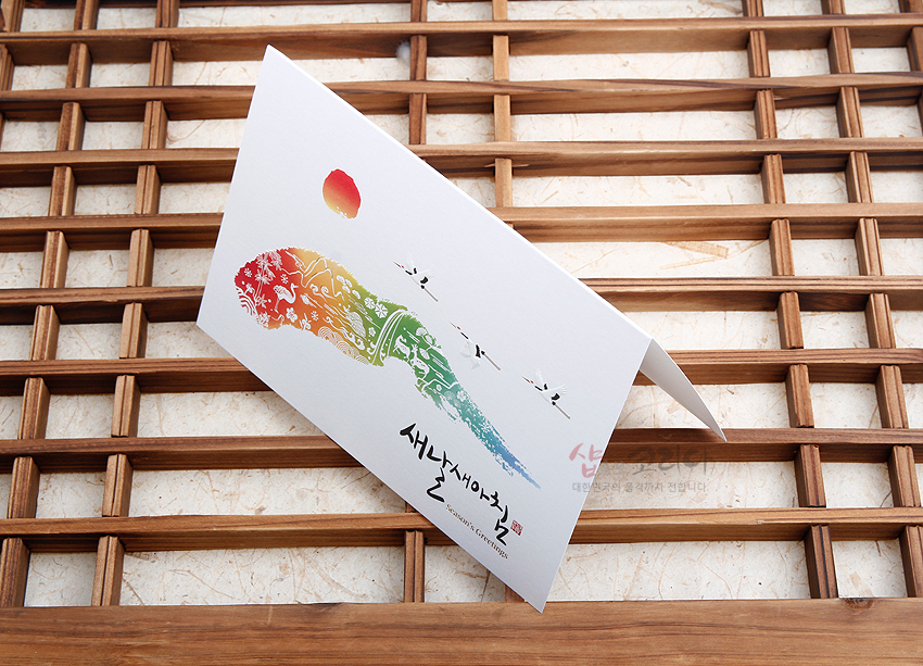 [텍스트: 새날새아침 SEASON'S GREETINGS] 한지 느낌의 카드 위에 붉은 해와 학, 구름, 산수 문양을 그라데이션 색채로 표현한 전통 일러스트 연하장 구성