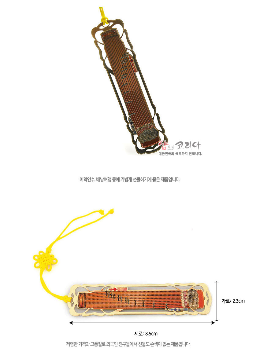 [텍스트: 샵오브코리아 대한민국의 품격까지 전합니다 / 세로: 8.5cm 가로: 2.3cm] 금장 금속틀 안에 적갈색 가야금 문양을 상감한 디자인과 노란 전통 매듭 끈이 조화를 이룬 책갈피 모습