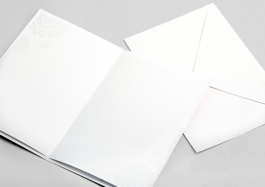[텍스트: 없음] 은은한 백색 한지 질감의 속지와 봉투 구성, 모서리에 압인된 연꽃·당초문 형태의 섬세한 음각 전통 문양 장식