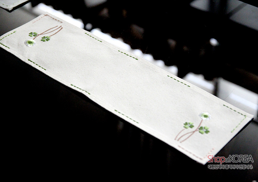 [텍스트: Shop of KOREA 대한민국의 품격, 가치를 전합니다] 광목 재질 아이보리 식탁보 위 초록 스티치 라인과 잔잔한 흰꽃, 연둣빛 잎사귀 자수 장식 이미지