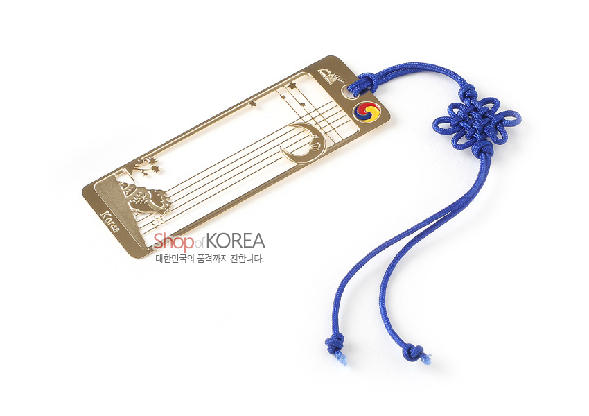[텍스트: Shop of KOREA, Korea] 금장 금속으로 달과 고동, 별 문양을 선으로 오픈워크한 직사각 책갈피와 청색 전통 매듭 끈 장식 구성