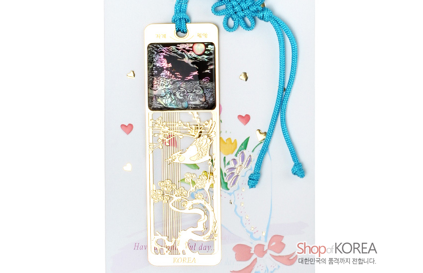 [텍스트: 기러기 원앙, KOREA] 금속 재질 위 자개 상감 기법으로 표현된 밤하늘과 원앙, 오픈워크 금장 매화 문양, 청색 전통 매듭 끈 장식의 책갈피 이미지 설명