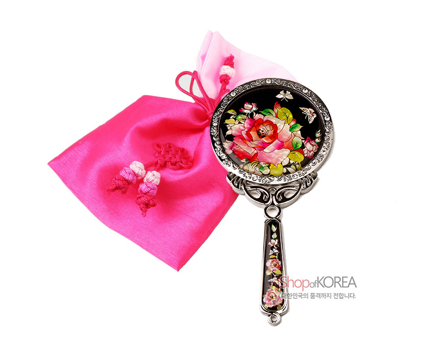 [텍스트: Shop of KOREA, 대한민국의 품격까지 전합니다.] 흑색 옻칠 바탕에 자개 상감으로 장미와 나비 문양을 넣고 금속 테두리와 손잡이를 장식한 손거울, 핫핑크 비단 주머니와 매듭 장식 구성