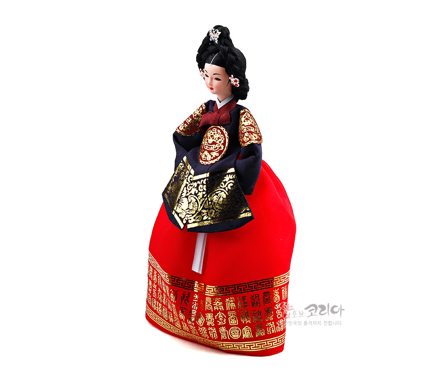 [텍스트: 샵오브코리아 한국의 품격까지 전합니다.] 붉은 비단 치마에 금색 문자·연속문단 장식, 남색 당의와 흉배에 금박 자수 보문이 수놓인 궁중 한복 인형 모습