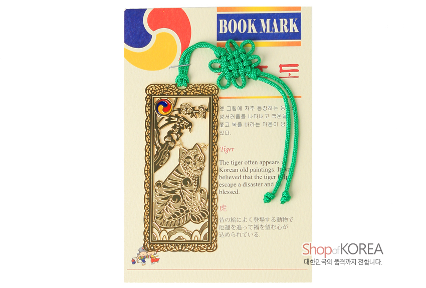 [텍스트: BOOK MARK / Tiger / Shop of KOREA 대한민국의 품격까지 전합니다.] 금속 재질 위 금장 처리된 직사각형 책갈피와 호랑이·까치 민화 문양, 삼태극 장식, 연두색 전통 매듭끈 구성 이미지 설명