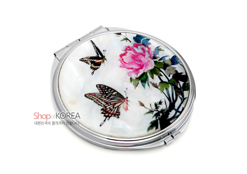 [텍스트: Shop of KOREA 대한민국의 품격까지 전합니다.] 흰 자개 바탕 위에 옻칠 처리된 분홍 모란과 나비 문양을 섬세한 채색으로 장식한 금속 테두리 원형 휴대 손거울 디자인