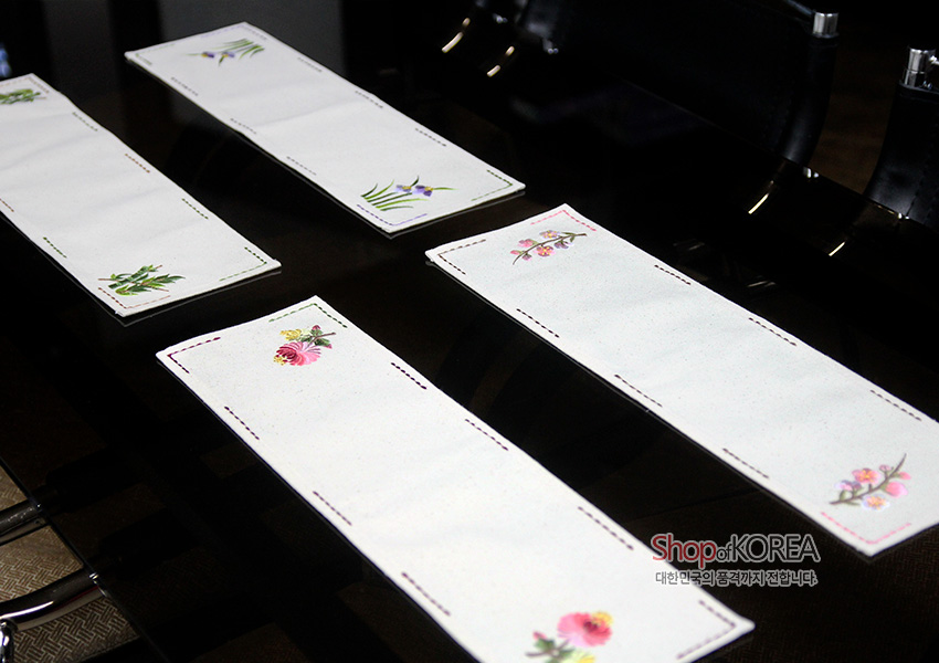 [텍스트: Shop of KOREA 대한민국의 공예가치 전달합니다] 광목 소재 직사각형 식탁보, 흰 바탕에 대나무와 꽃 등 전통 식물 자수와 컬러 스티치 라인 장식 디자인
