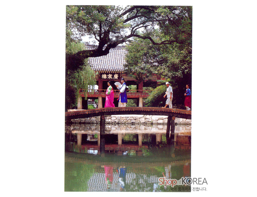 [텍스트: Shop of KOREA, 대한민국의 품격까지 전합니다.] 전통 한옥과 기와지붕, 나무다리 위 형형색색 비단 한복 인물, 연못 수면에 비친 풍경 대비 이미지