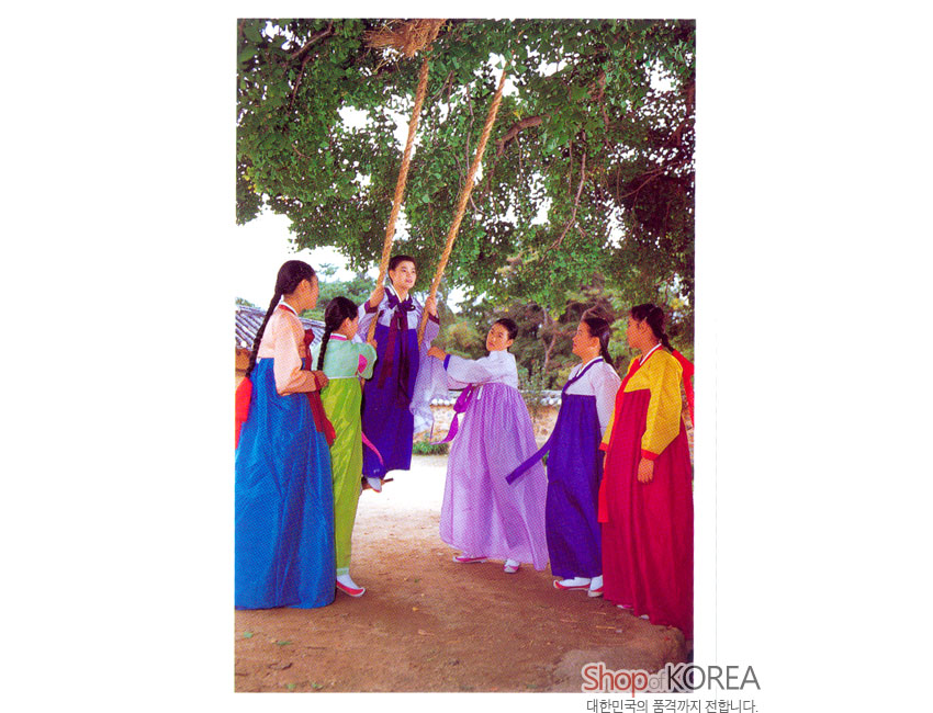[텍스트: Shop of KOREA 대한민국의 품격까지 전합니다.] 푸른 수풀 아래 자연 섬유로 엮은 그네, 오방색 비단 한복 치마저고리를 입은 인물들의 전통 그네뛰기 풍경 엽서 모습