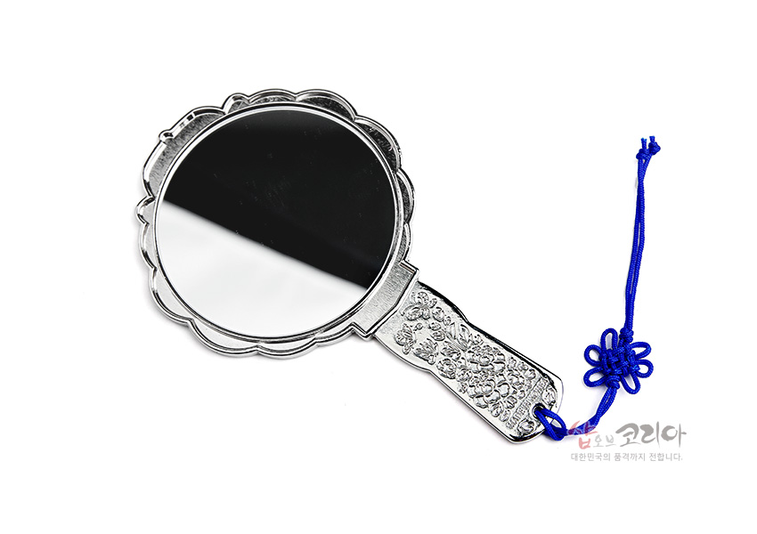 [텍스트: 샵오브코리아 대한민국의 품격까지 전합니다.] 금속 재질에 정교한 꽃 문양을 양각한 손잡이와 은색 테두리, 청색 전통 매듭끈 장식이 돋보이는 원형 손거울 이미지 설명