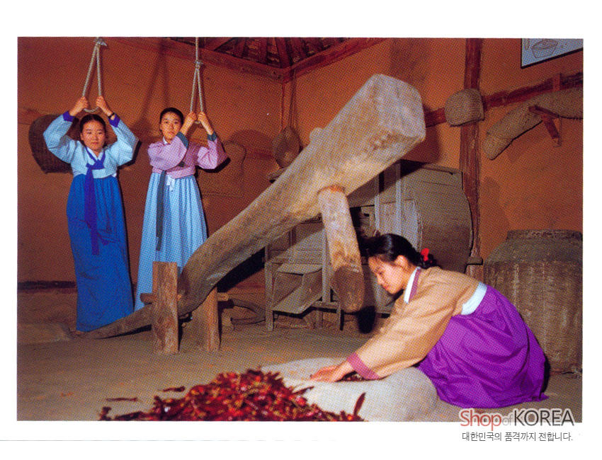 [텍스트: Shop of KOREA 대한민국의 품격까지 전합니다.] 한옥 실내 디딜방아와 짚공예 도구를 배경으로, 청색·보라색 비단 한복을 입은 여인들의 전통 농경 작업 풍경 이미지
