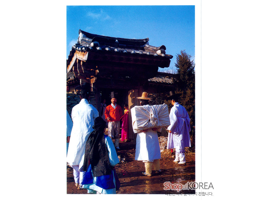 [텍스트: Shop of KOREA] 전통 기와문과 돌담을 배경으로 흰색·남색·홍색 비단 한복을 갖춰 입은 인물들이 보자기 짐을 들고 서 있는 한국 옛 풍경 엽서 이미지