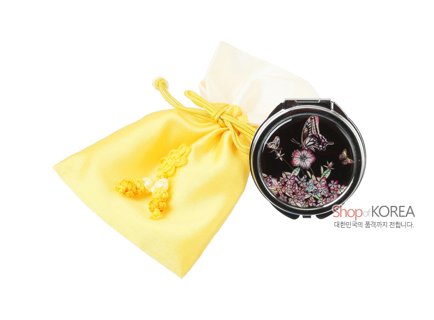 [텍스트: Shop of KOREA 대한민국의 품격까지 전합니다.] 검은 바탕 금속 원형 자개 손거울의 나비·꽃 상감 문양과 노랑 비단 매듭 복주머니 구성 이미지 묘사