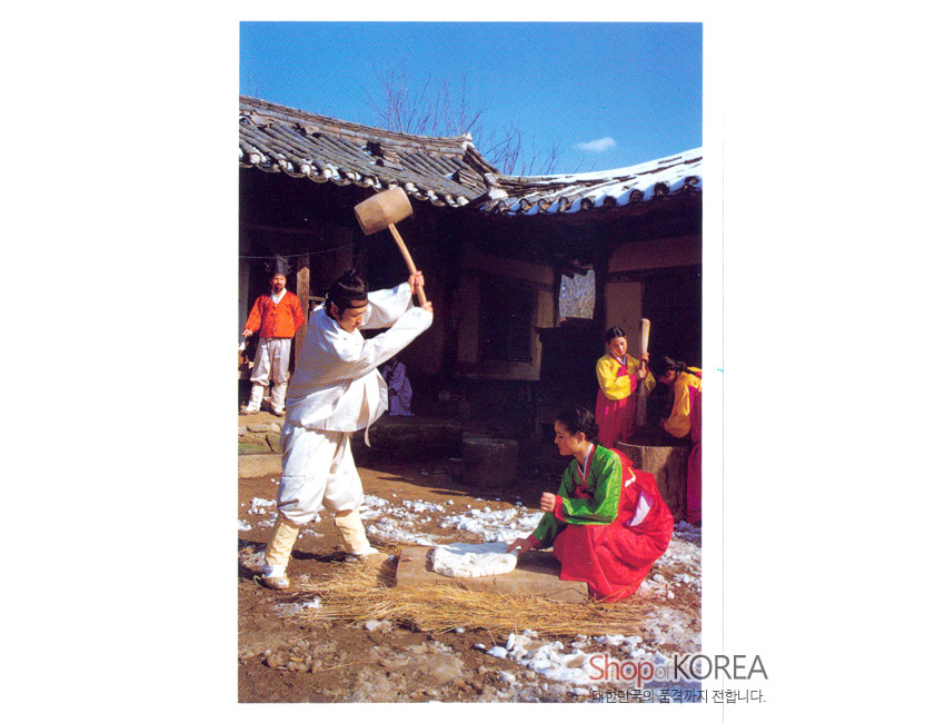 [텍스트: ShopKOREA 대한민국의 품격까지 전합니다.] 한옥 마당 설경 속 전통 의상 인물들의 떡 치기 장면, 흰 눈과 기와지붕 대비가 돋보이는 사진 엽서 디자인
