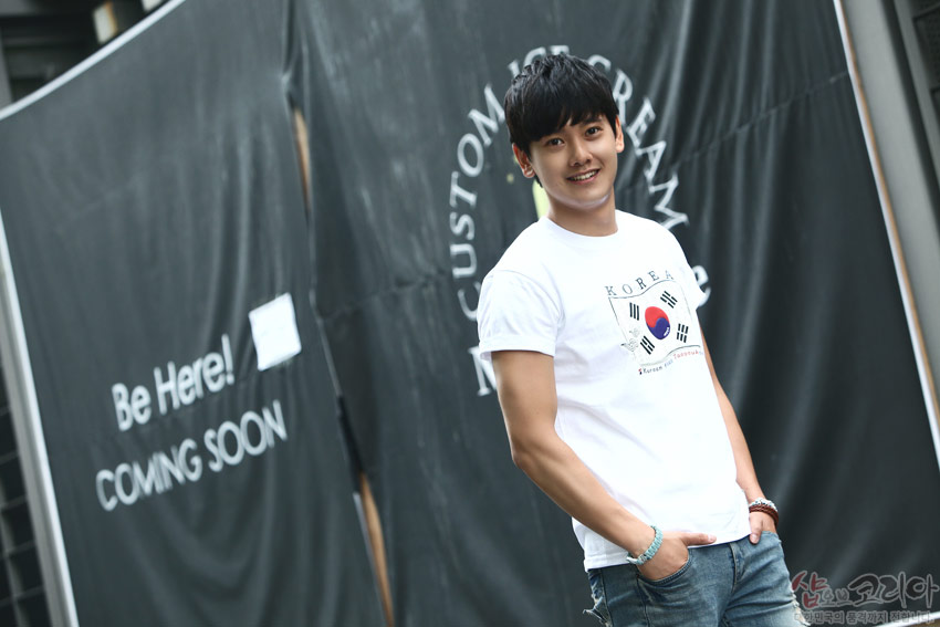 [텍스트: Be Here! COMING SOON / KOREA] 흰색 면 티셔츠 중앙 태극기와 사괘, 영문 텍스트가 입체 발포 기법으로 인쇄된 현대적 전통 문양 디자인