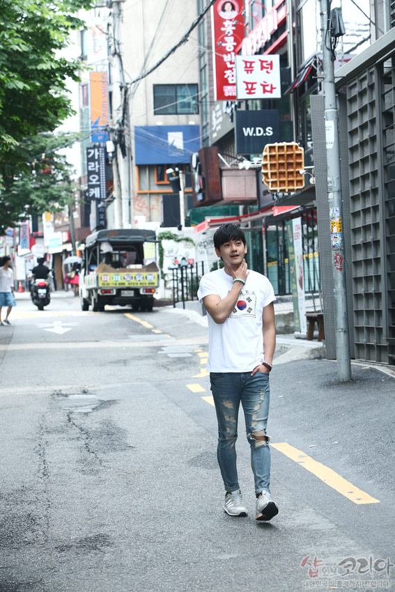 [텍스트: 샵오브코리아 대한민국 전통문화상품] 흰색 면 반소매 티셔츠에 태극 문양과 사괘를 입체 발포 기법으로 표현한 캐주얼 연출 거리 풍경 이미지