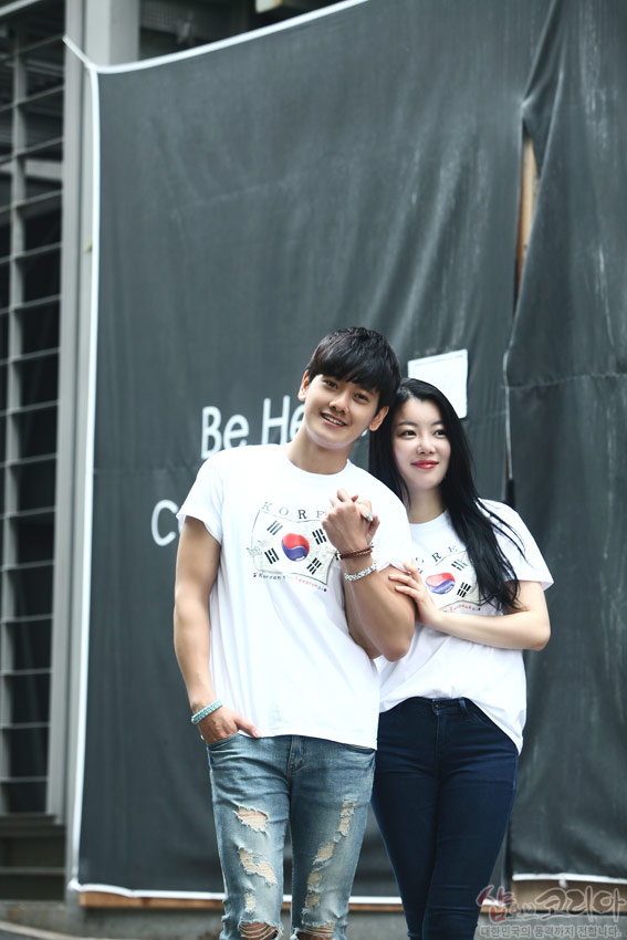 [텍스트: Be Hea…, KOREA, In Korea I fell in love, 샵오브코리아 대한민국의 전통과 기념품의 만남] 흰색 면 소재에 태극기와 사괘, 원형 입체발포 기법으로 표현된 전통 문양 티셔츠를 입은 커플 모습