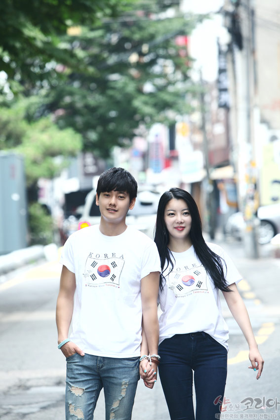 [텍스트: KOREA, Korean Folk Tradition] 흰색 면 반소매 티셔츠에 태극기 문양과 사괘를 3D 입체발포 기법으로 표현한 커플 착용 거리 풍경 이미지