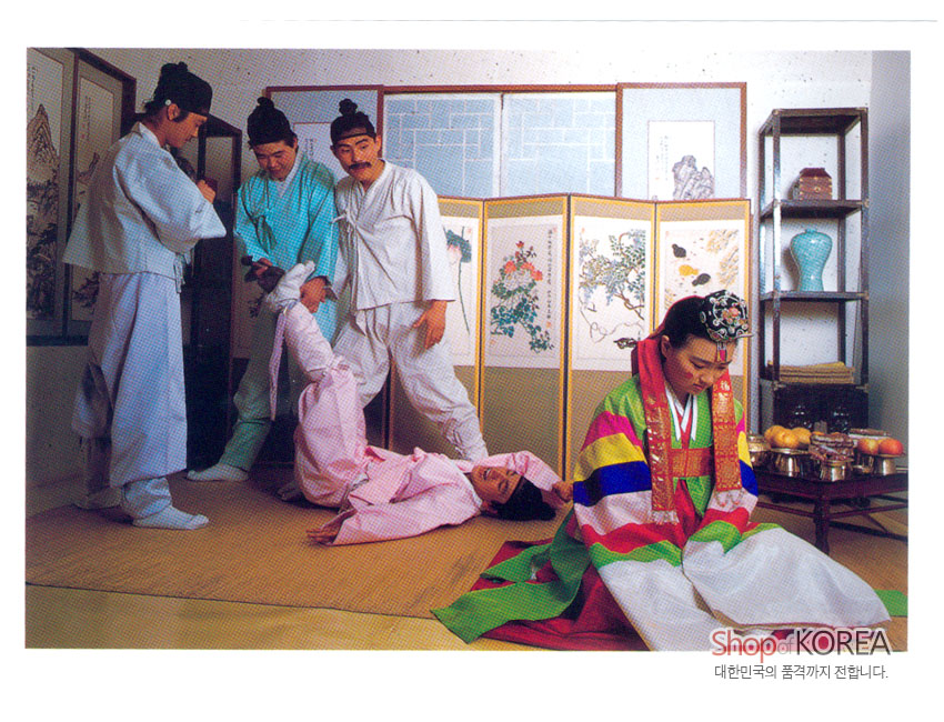 [텍스트: Shop of KOREA / 대한민국의 품격까지 전합니다.] 오방색 비단 혼례복과 금박 장식 족두리, 민화 병풍과 청자 장식이 어우러진 실내 혼례 풍경 이미지