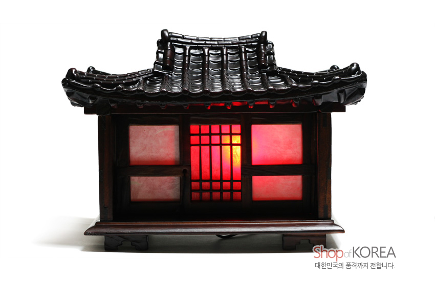 [텍스트: Shop of KOREA 대한민국의 품격까지 전합니다.] 어두운 목재 기와지붕과 창살 문양, 반투명 적·백색 패널에서 퍼지는 따뜻한 주황빛 조명 연출
