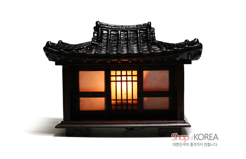 [텍스트: Shop of KOREA 대한민국의 품격까지 전합니다.] 짙은 갈색 목조 기와지붕과 창살 무늬, 반투명 적백색 패널에서 따뜻한 주황빛이 새어 나오는 한옥 형 좌등 스탠드 조명 연출