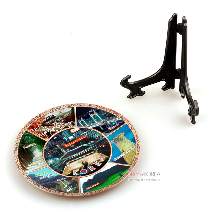 [텍스트: Sungnyemun, KOREA, Hahoe Village, Korea, Seorak Mountain, Busan, Cheomseongdae Observatory, ShopofKOREA 대한민국의 품격까지 전합니다.] 금속 재질 원형 접시에 한국 풍경 컬러 인쇄와 전통 문양 테두리, 검정색 플라스틱 접시 거치대 구성 장식품