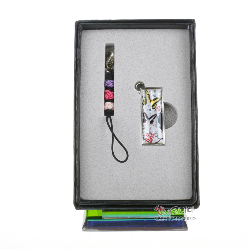 [텍스트: 샵오브코리아 대한민국의 품격까지 전합니다.] 금속 테두리 자개 장식 직사각 USB와 노랑·보라·분홍 매듭 실 스트랩이 함께 놓인 패키지 구성 이미지
