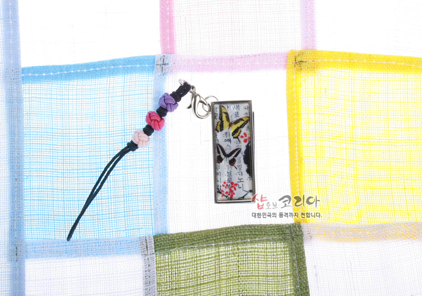 [텍스트: 샵오브코리아 대한민국의 품격까지 전합니다.] 금속 테두리 직사각 USB에 한글 서체 배경과 노랑·검정 나비, 붉은 매화가 채색되고 매듭 장식 스트랩이 더해진 디자인