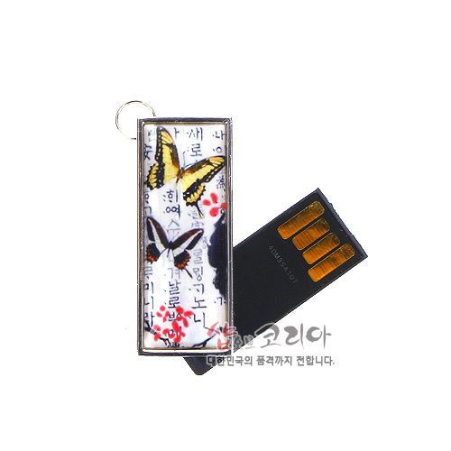 [텍스트: 샵오브코리아 대한민국의 품격까지 전합니다.] 금속 테두리 직사각 케이스에 한글 서체 배경, 노랑·검정 매화나비와 붉은 매화 문양을 채색한 USB 메모리 장식 이미지 설명