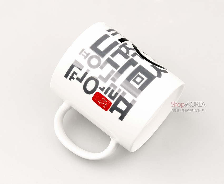 [텍스트: Shop of KOREA 대한민국의 품격까지 전달합니다] 백색 도자 머그컵 표면에 회색과 검은색 한글 자모가 격자형으로 배열되고 붉은 인장 문양이 포인트로 들어간 그래픽 디자인 이미지 설명