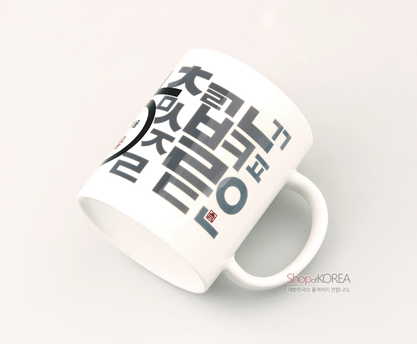 [텍스트: ShopofKOREA 대한민국의 품격까지 전합니다.] 백색 도자기 머그컵에 회색 한글 자모와 붉은 낙관, 검은 반원형 문양이 조형적으로 배치된 디자인