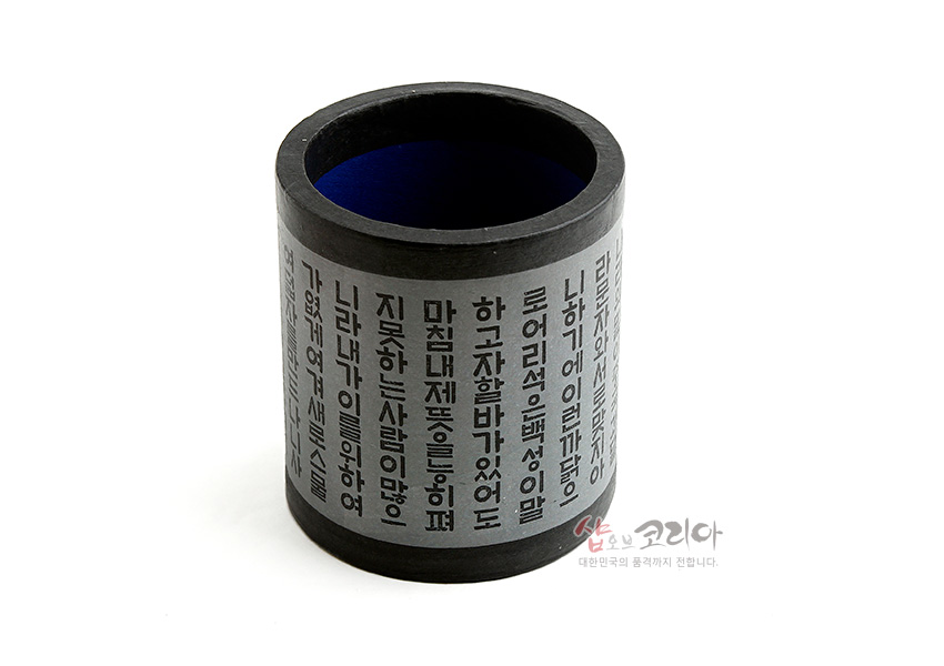 [텍스트: 나랏말싸미 듕귁에 달아 문자와로 서로 사맛디 아니할쎄 이런 젼차로 어린 백성이 니르고져 할빼이셔도 마참내 제 뜻을 능히 펴디 몯할 놈이 하니라] 검정 테두리와 청색 내부가 어우러진 종이 재질 원통형 펜꽂이, 세로 배열 훈민정음 서체 인쇄 디자인 특징