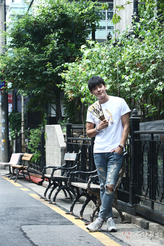 [텍스트: 샵오브코리아] 흰색 순면 반팔 티셔츠에 다색 3D 입체발포 기법으로 표현된 풍물놀이 문양, 거리 풍경과 조화를 이루는 캐주얼 연출 모습