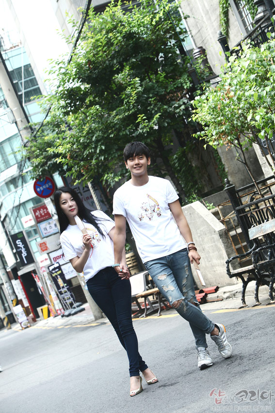 [텍스트: 샵오브코리아] 흰색 순면 반팔에 다색 3D 입체발포 기법으로 표현한 풍물놀이 전통무늬 장식 티셔츠 착용한 거리 연출 이미지