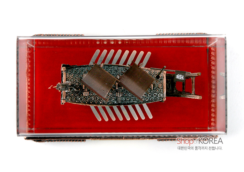 [텍스트: Shop of KOREA / 대한민국의 품격까지 전합니다.] 붉은 벨벳 바탕 위 청동색 금속 재질로 정교하게 조각된 거북선 모형과 투명 아크릴 케이스가 조화를 이룬 상단 장식 이미지