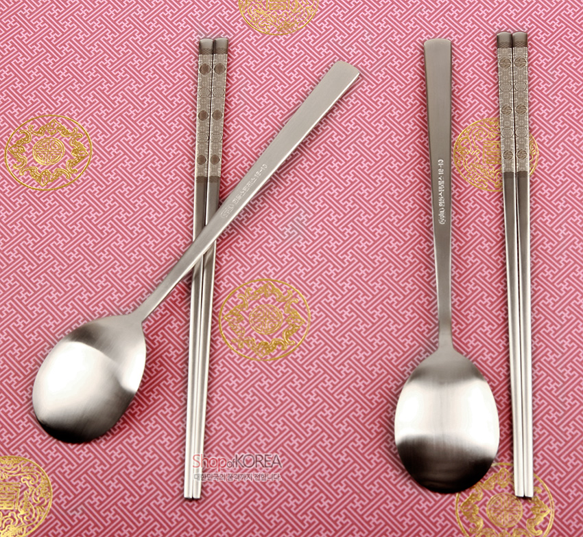 [텍스트: ShopofKOREA] 은빛 금속 재질에 젓가락 손잡이 부분 십장생 문양 레이저 음각 장식, 전통 문양 분홍 바탕 위 배치된 2인 수저 세트 이미지 설명