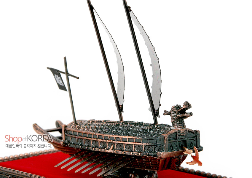 [텍스트: Shop of KOREA 대한민국의 품격까지 전합니다.] 청동색 금속으로 정교하게 표현된 거북선 선체와 용두 장식, 검은 돛과 깃발, 붉은 벨벳 바탕이 대비되는 전통 선박 모형 장식품 모습