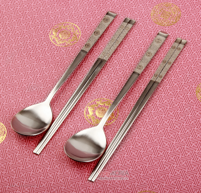 [텍스트: ShopofKOREA] 분홍색 전통 기하 문양 바탕에 금색 원형 문양 장식, 손잡이에 십장생 문양을 정교하게 레이저 각인한 은빛 금속 수저와 젓가락 2인 세트 이미지 설명