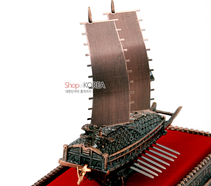 [텍스트: Shop of KOREA 대한민국의 품격까지] 청동색 금속 재질로 조각된 거북선 모형과 미세 격자 무늬 돛, 붉은 벨벳 천 바닥이 어우러진 전통 선박 장식 이미지